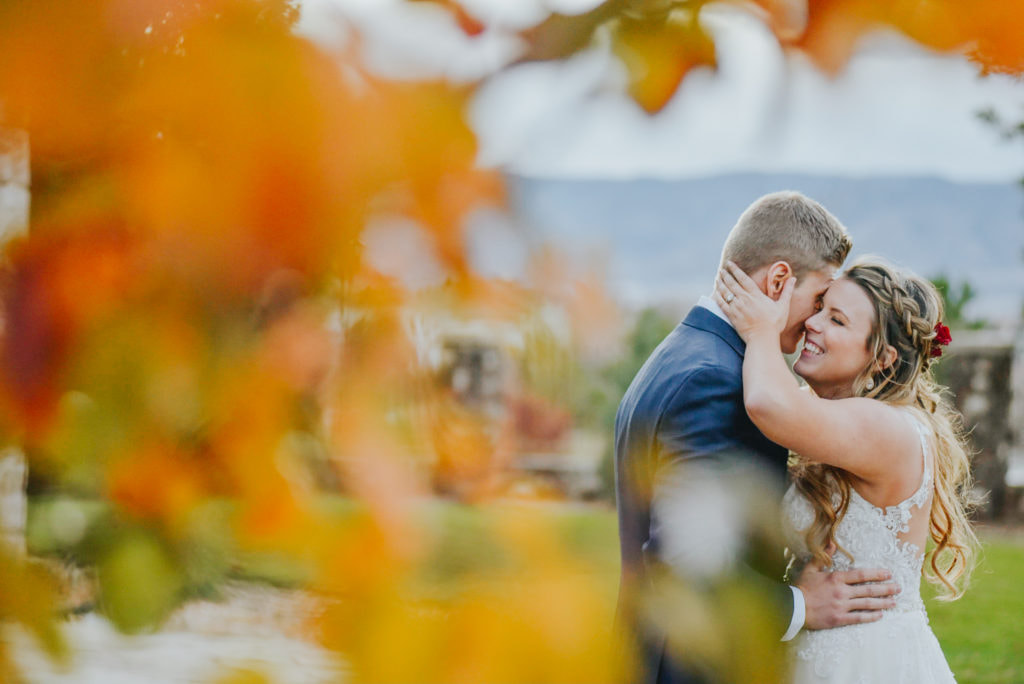 bride and groom embracing as seen through the fall leaves