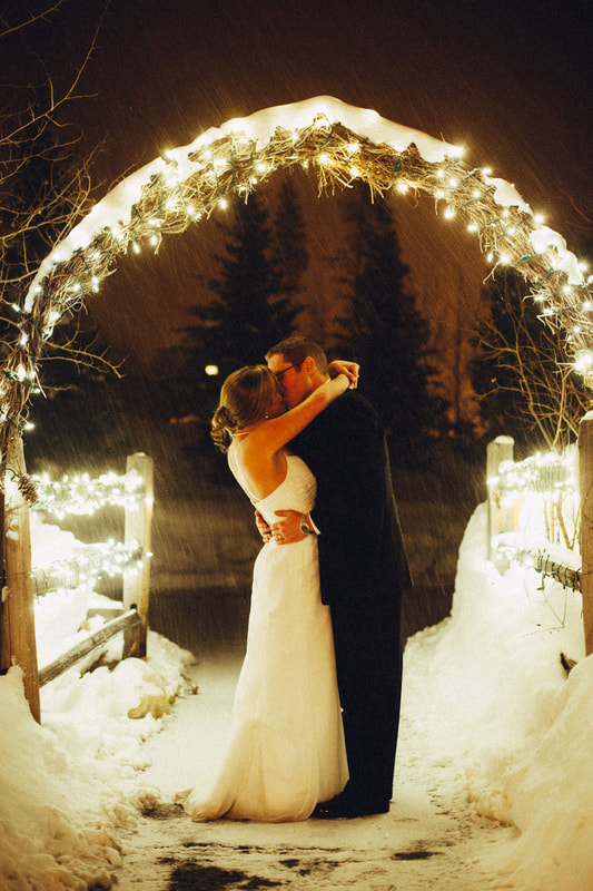 bride and groom kissing under a twinkle light lit wooden alter