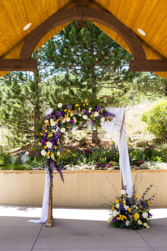 Wedding ceremony arch with purple, yellow, and cream flowers by Earth Tones Floral