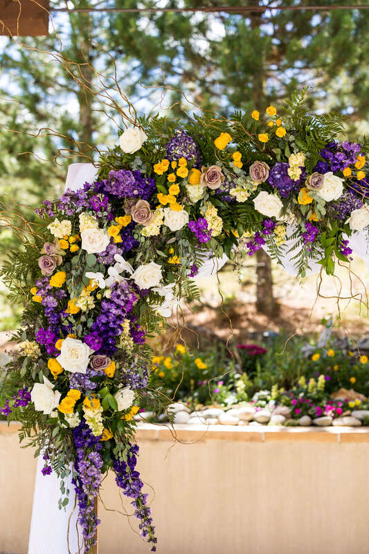 Wedding ceremony arch with purple, yellow, and cream flowers by Earth Tones Floral