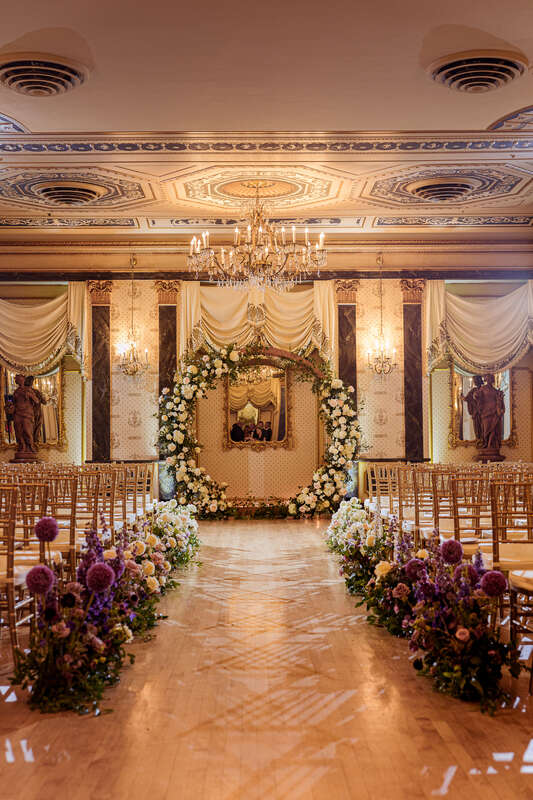 A round arch covered in ivory roses and greenery for an indoor wedding ceremony