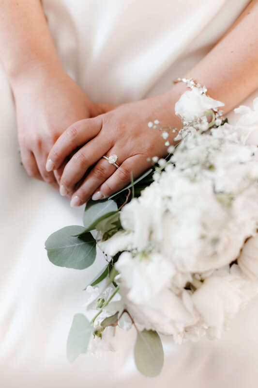Bride wearing an oval diamond engagement ring holding a white wedding bouquet