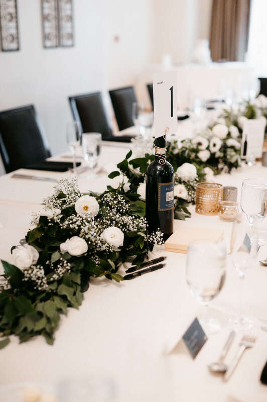 Long floral centerpiece with greenery and white flowers on a wedding table