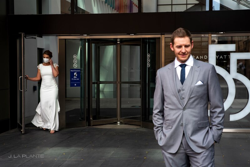 downtown denver COVID wedding as bride exits the hotel with bridal face mask behind the groom
