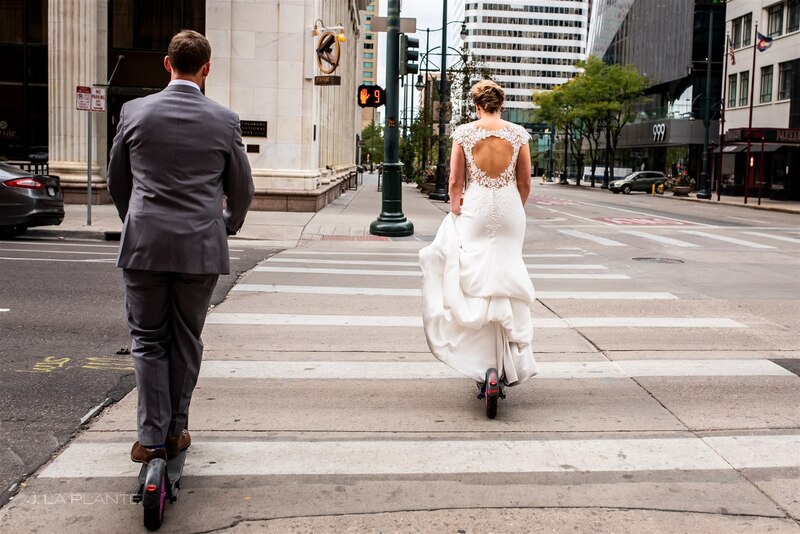 following bride and groom through downtown denver crosswalk on electric scooters