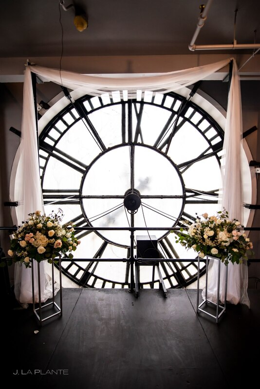 clocktower clock faces backdrop to the white draped altar with white rose and greenery floral arrangements