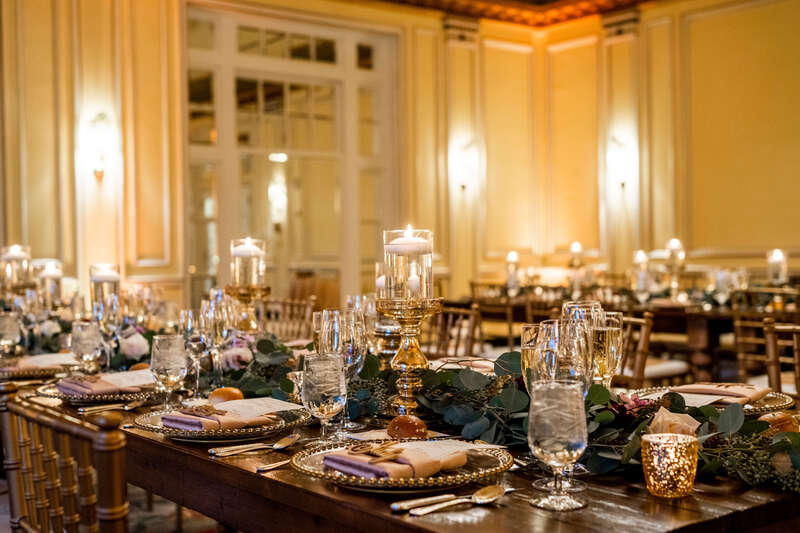 Floating candles, gold-rimmed chargers, and greenery for a winter wedding reception