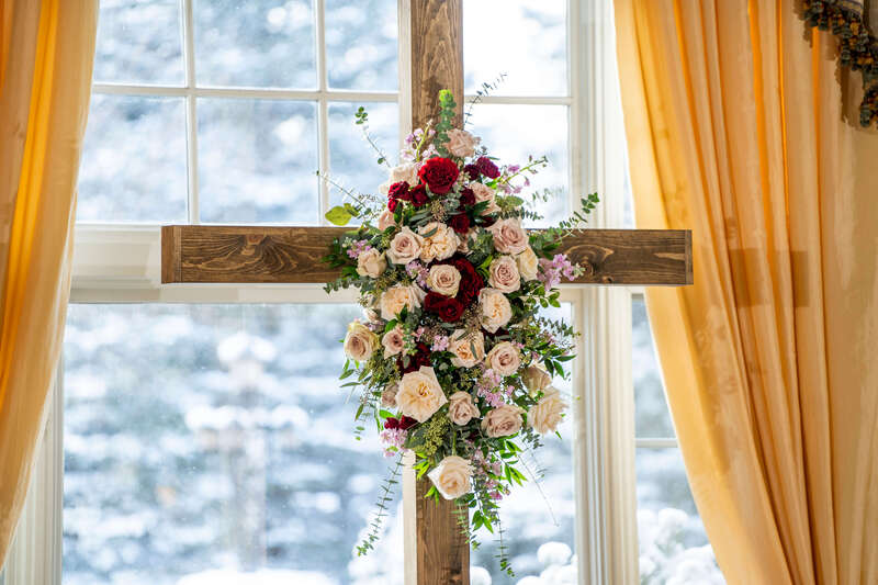 A handmade wooden cross decorated with red and blush roses for a winter wedding ceremony