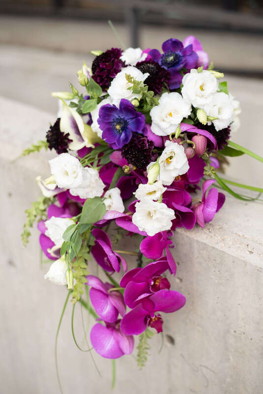 A purple and white bridal bouquet filled with orchids, pansies, and lisianthus by Newberry Brothers