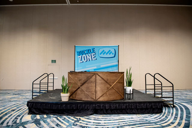 Stage set up with custom backdrop, wooden bar, and potted plants