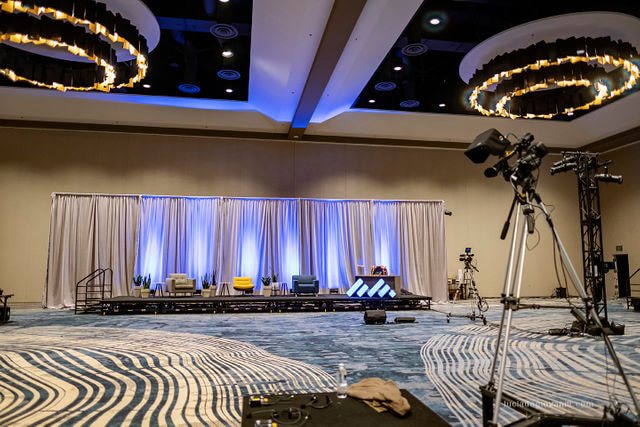 Long stage set with draping, uplighting on draping and view from behind the live streaming camera
