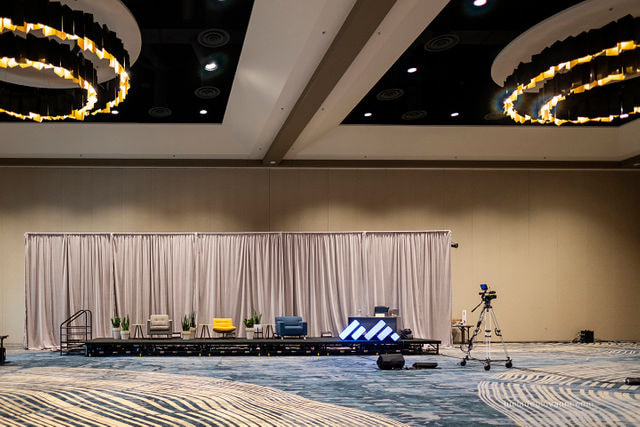 Long stage with draping with furniture on the stage and placement of an up-close live stream camera