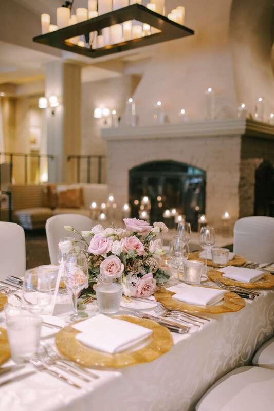 White linens, gold chargers, and pink floral centerpieces for a romantic wedding reception