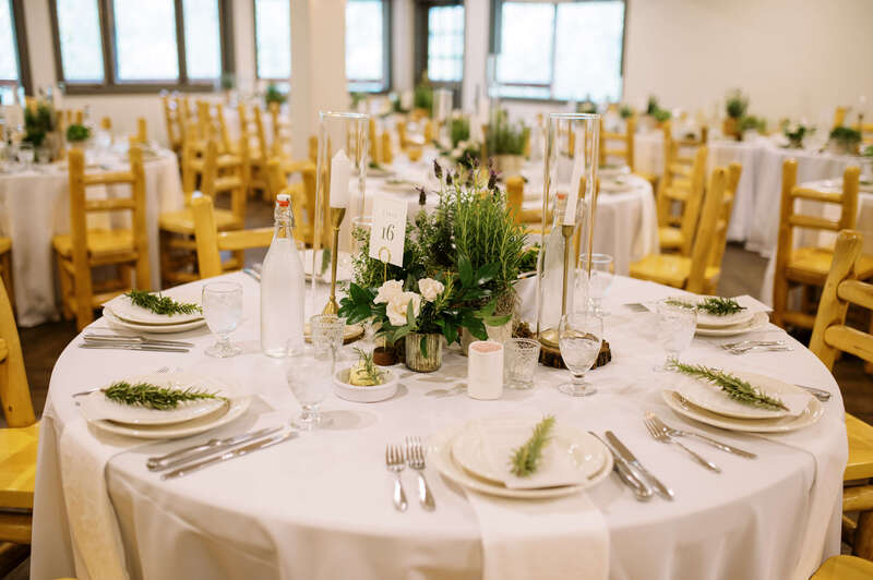 White table linens and plates topped with sprigs of rosemary for a wedding reception