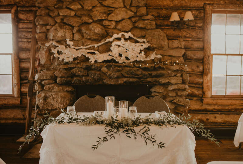 Sweetheart table in front of a stone fireplace with white candles and eucalyptus