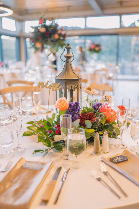 Tables with white linens, gold accents, and colorful floral centerpieces at a wedding reception