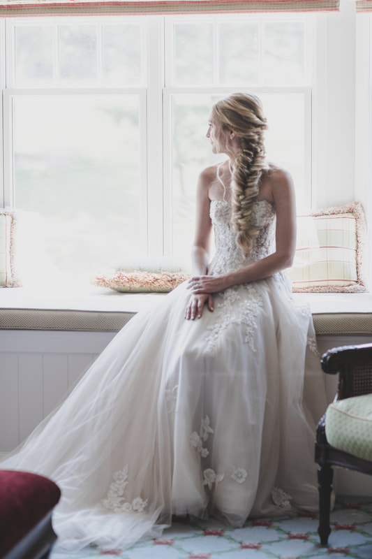 Bride looking out the bay window and spotlighting her long, fishtail braid