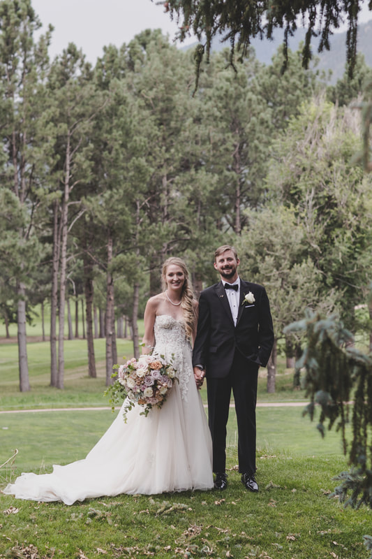 Bride and groom holding hands and smiling for the camera amongst the trees and green lawns