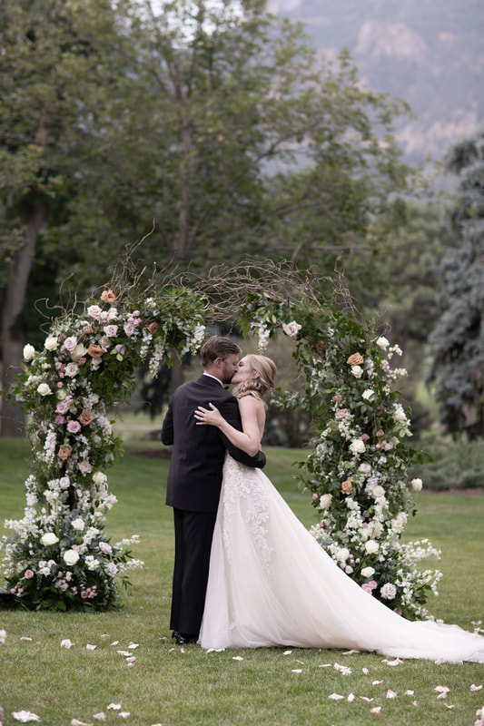 Bride and Groom first kiss underneath their floral wedding arch
