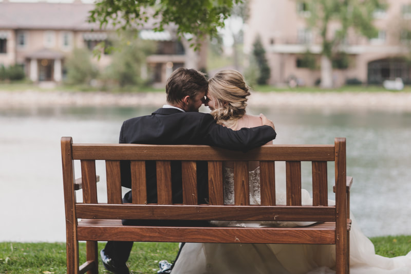 Bride and groom on a wooden park bench with the Broadmoor Lake in the background