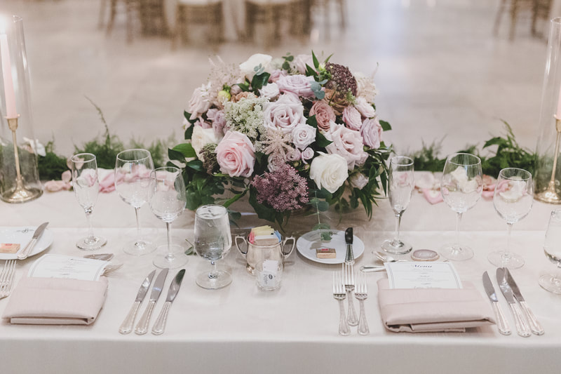 Sweetheart table centerpiece with light purple, light pink, and white roses accompanied with greenery