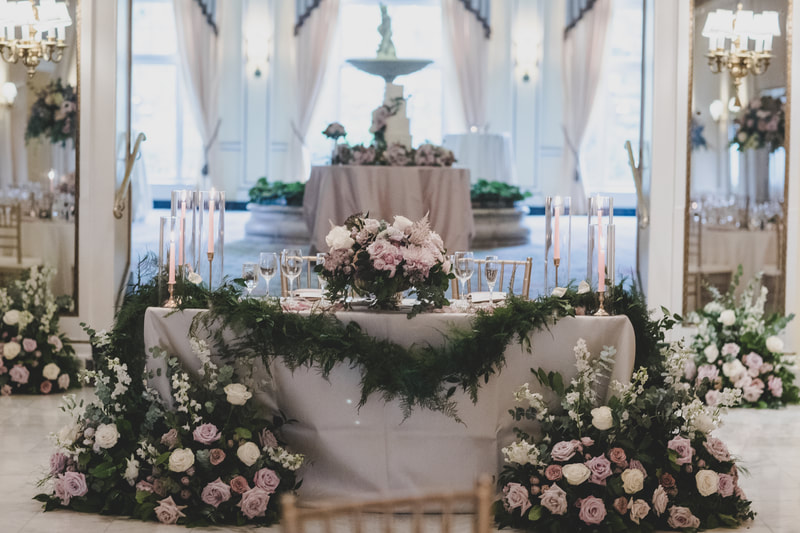 front of the sweetheart table with two floral arrangements on each side and draped with greenery