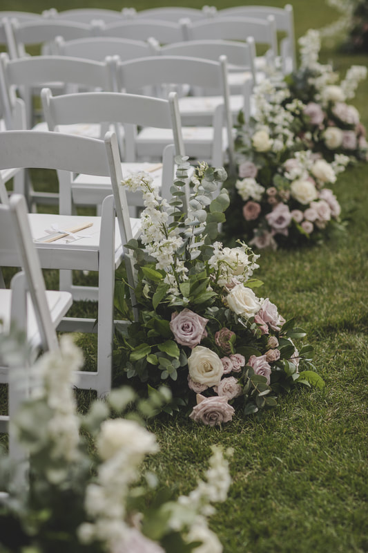 Wedding aisle floral arrangements next to guest chairs